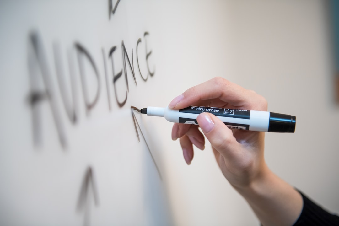 La main d'une femme écrit le mot audience sur un tableau blanc, avec des flèches.